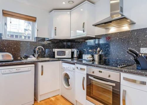 a kitchen with white cabinets and a washer and dryer at House 6 Goldcroft - Walk to Beach & Village, Pet-friendly & hottub in Porthtowan