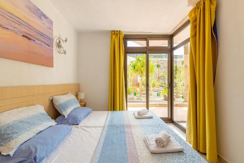 a bedroom with a bed and a window with yellow curtains at SeaBliss Beach of Dunes, Terrace and Pool! in San Bartolomé