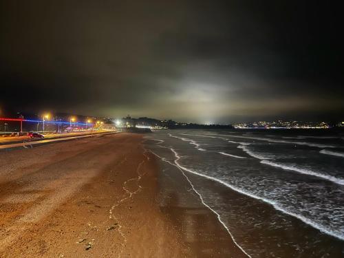 una playa vacía por la noche con luces en el océano en The Commodore Rooms & Relaxation, en Paignton