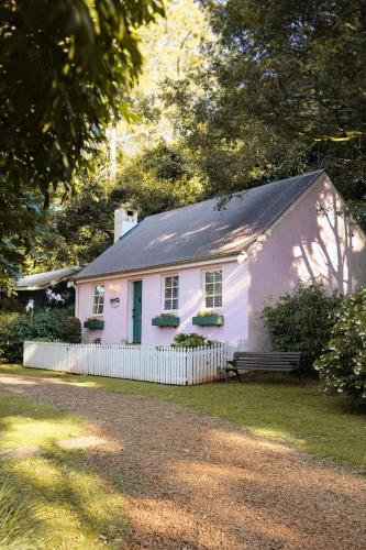 a white house with a bench in front of it at The Romantic Pink English Cottage at Tamborine Mountain in Mount Tamborine