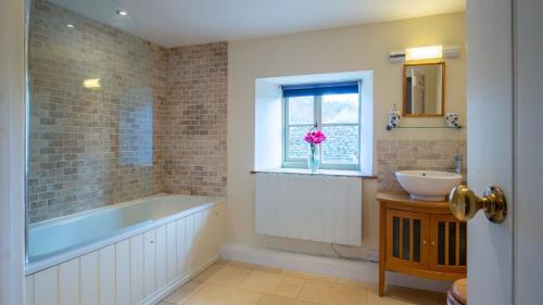 a bathroom with a tub and a sink and a window at Hope Cottage in Naunton