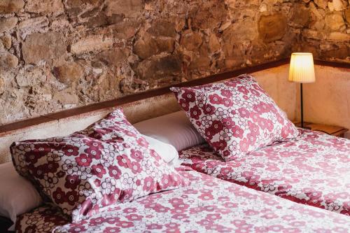 a bed with red and white pillows next to a stone wall at Mas Teixidor in Crespiá