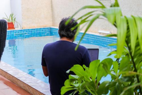 a man sitting next to a swimming pool with a laptop at Ari Grand Hotel & Spa in Dhangethi