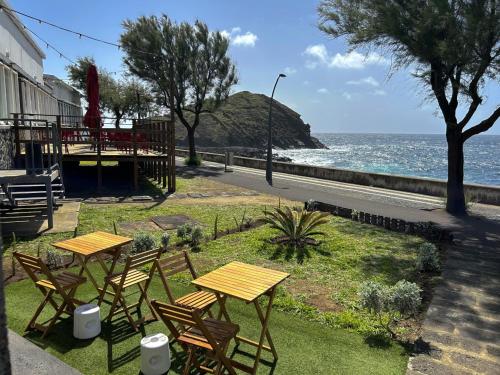 two tables and chairs sitting next to the ocean at Cantinho do Ilhéu in Ponta Delgada