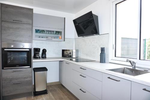 Il comprend une cuisine avec des placards blancs, un évier et une télévision. dans l'établissement Maison à 300m de la plage, Classée 3 étoiles - Le Crotoy, au Crotoy
