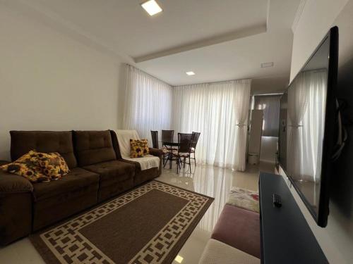 a living room with a brown couch and a television at Apartamento Novo e Confortável in Itapema