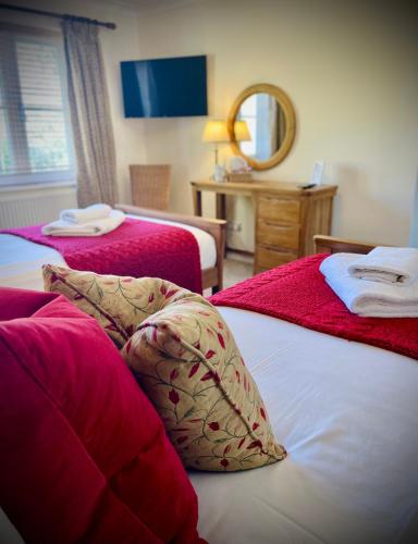 a bedroom with two beds with red sheets and a mirror at The Crown Inn in Rodmarton