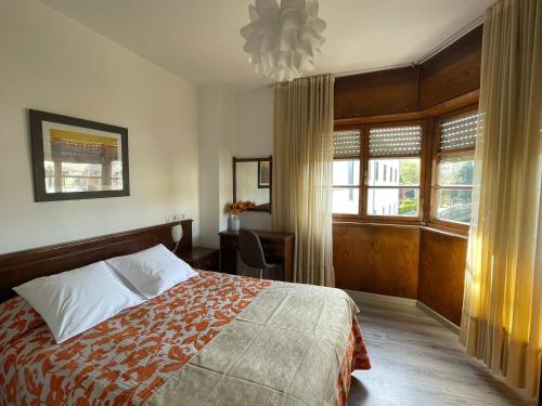 a bedroom with a bed and a desk and windows at Hotel La Bilbaina de Vegadeo in Vegadeo