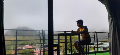 a man sitting on a balcony looking out a window at Foggy Mount View in Bandarawela