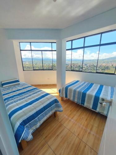 two beds in a room with large windows at Disha's Home Casa Hospedaje in Ayacucho