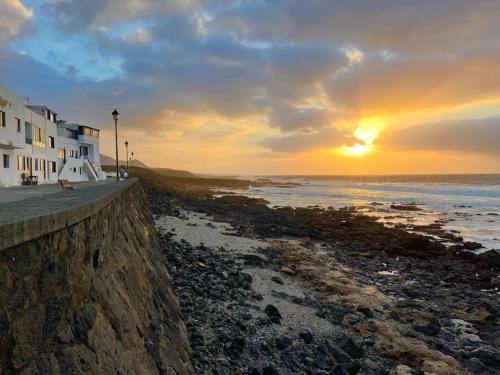 - un coucher de soleil sur une plage avec un bâtiment et l'océan dans l'établissement Weybeach2 -shared terrace,plaza view,sea frontline, à La Santa