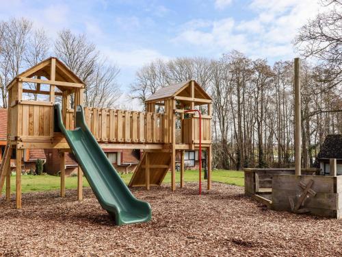 a playground with a green slide and a wooden house at Lilyrose Cottage in Pevensey