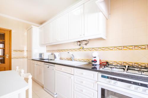 a white kitchen with white cabinets and a sink at Frente ao Mar - 2 quartos - wi-fi in Armação de Pêra