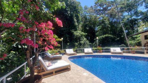 a swimming pool with chairs and pink flowers next to it at ECOTICA Boutique Hotel in Manuel Antonio