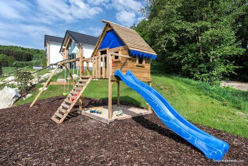 um parque infantil de madeira com escorrega e uma casa em Panoramabungalow _50_ im Feriendor em Truppach