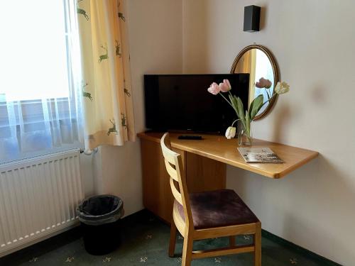 a desk with a television and a vase of flowers on it at Posthotel Pfunds in Pfunds