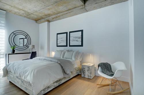 a white bedroom with a large bed and a chair at Les Immeubles Charlevoix - Le 760608 in Quebec City
