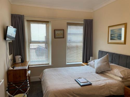 a bedroom with a bed and a desk and two windows at Bron Menai Guest House in Caernarfon