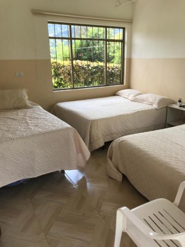 a room with two beds and a window and a chair at Finca Marandua Cabaña El Cielo in Pacho