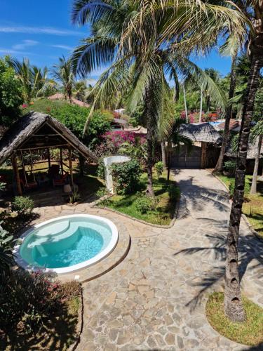 a swimming pool next to a resort with a palm tree at Waridi House in Watamu