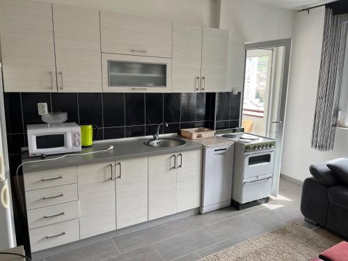 cocina con armarios blancos, fregadero y microondas en STAN 54m2, en Priboj