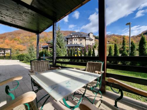 a table and chairs on a porch with a view of a house at PLANINSKO JUTRO - Brzeće Centar Apartments, Kopaonik in Brzeće