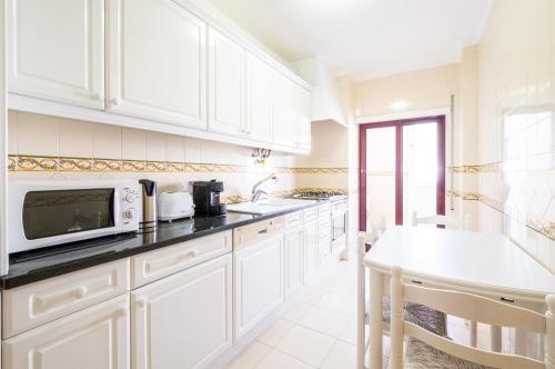 a kitchen with white cabinets and a microwave at Frente ao Mar - Sea Front - 3 Quartos - wi-fi - Algarve in Armação de Pêra