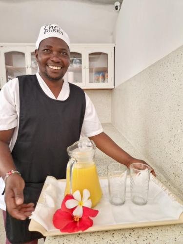 a man standing in a kitchen holding a tray of juice at Waridi House in Watamu