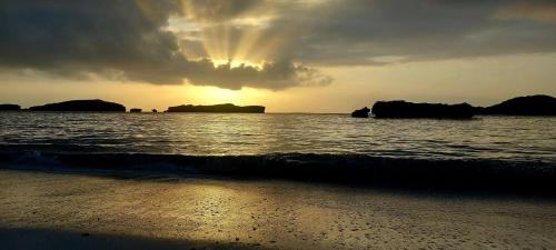 a sunset on the beach with the ocean and rocks at Waridi House in Watamu