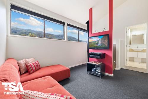 a living room with a red couch and a tv at Mowamba E5 in Thredbo