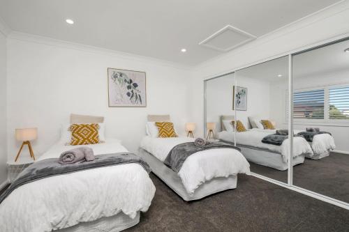 2 Betten in einem weißen Zimmer mit Spiegeln in der Unterkunft Newly Built Spacious Beach Home in The Entrance