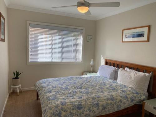 a bedroom with a bed with a ceiling fan and a window at The Sands in Mollymook