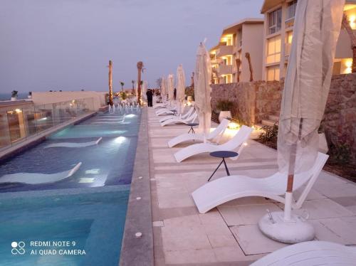 eine Reihe weißer Stühle neben einem Pool in der Unterkunft Il monte galala Sea view Chalet المونت جلاله in Ain Suchna
