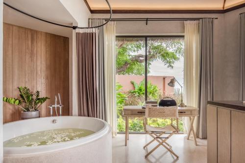 a bathroom with a tub and a desk and a window at VALA Hua Hin - Nu Chapter Hotels in Cha Am