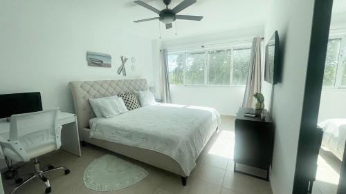 a white bedroom with a bed and a ceiling fan at Sunny Caribbean Apartment with Pool in Punta Cana