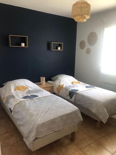 une chambre avec deux lits et un mur bleu dans l'établissement Les Ecrehous de Saint Jean, à Barneville-Plage