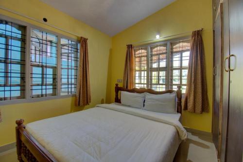 a bedroom with a bed with yellow walls and windows at Green Land Estate Homestay 5 Rooms With Garden View in Madikeri