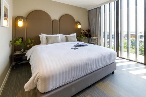 a large white bed in a room with large windows at Benjarong Hotel Bangkok in Ban Zong Katiam