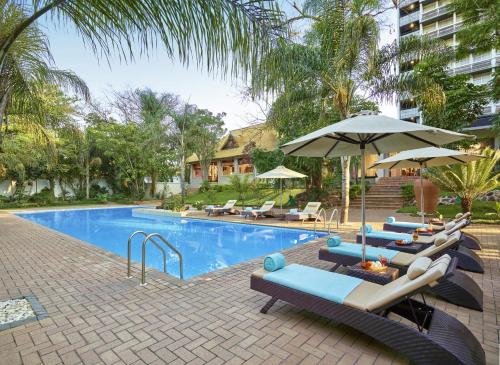 a pool with chairs and umbrellas next to a building at Taj Pamodzi Lusaka in Lusaka