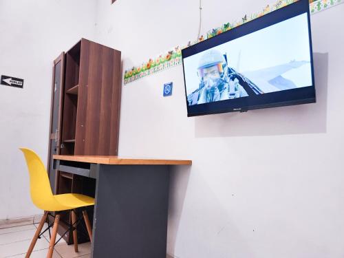 a television hanging on a wall with a table and a chair at Homey Guesthouse Kertajaya (Syariah) in Surabaya