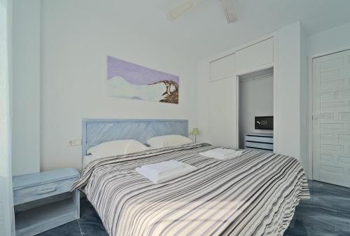 a white bedroom with a large bed with a striped blanket at All Suite Ibiza Aparthotel in San Antonio
