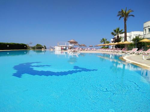 a large blue swimming pool with chairs and palm trees at Yalikavak Holiday Gardens in Yalıkavak