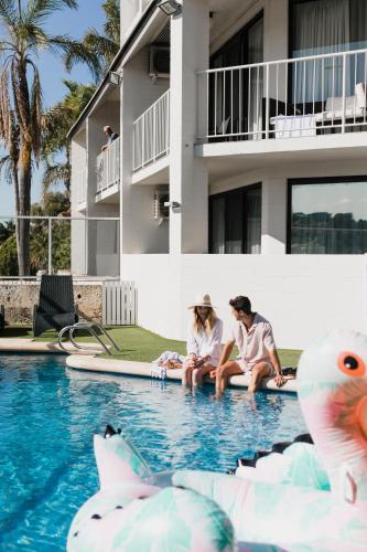 two people sitting on the edge of a swimming pool at Pier 21 Riverside Apartment Hotel in Fremantle