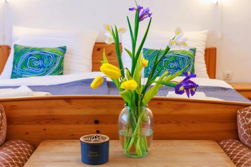 a vase with flowers on a table in front of a bed at Retel Vitez Vendégház in Sárospatak