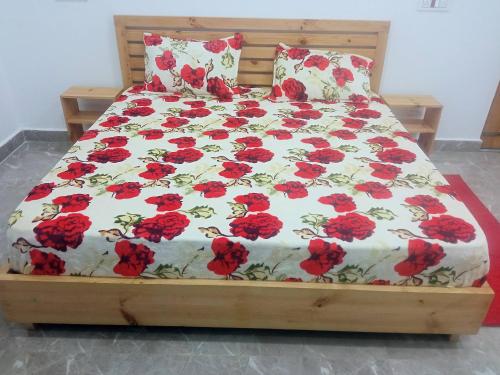 a bed with a red and white comforter with red flowers at Travelodge Homestay in Bīr