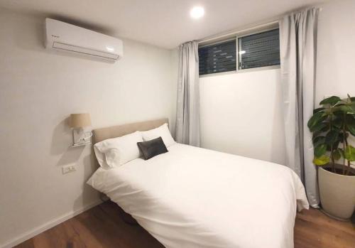 a white bedroom with a white bed and a plant at Assuta Residence in Ramat HaHayal, Tel Aviv in Tel Aviv