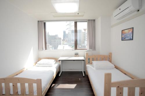 two beds in a room with a desk and a window at ゲストハウス昴 in Tokyo