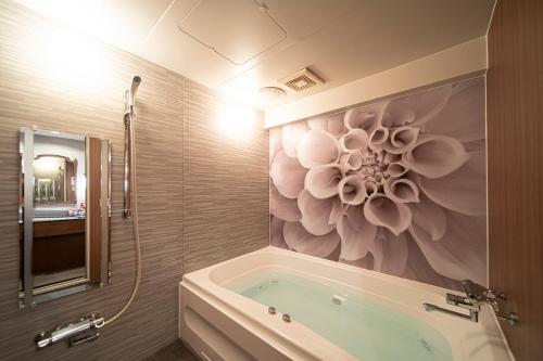 baño con bañera con una pintura floral en la pared en ホテル リッド 男塾ホテルグループ en Hikone