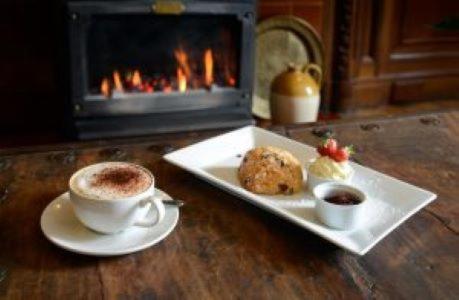 a cup of coffee and cookies on a table with a fireplace at Mabie House Hotel in Dumfries