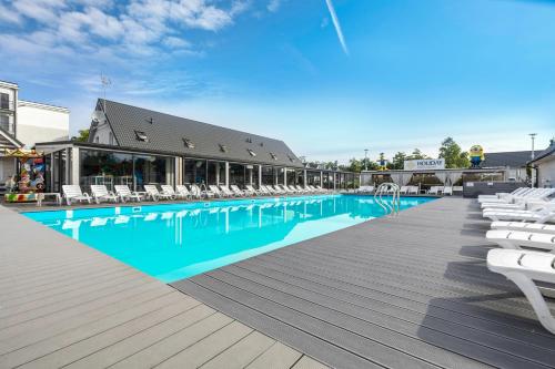 a large swimming pool with white chairs next to a building at Holiday Park & Resort Ustronie Morskie in Ustronie Morskie